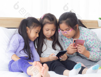 快乐亚洲孩子朋友玩智能手机沙发首页孩子们电话沙发上女孩看聪明的电话娱乐生活方式沟通概念