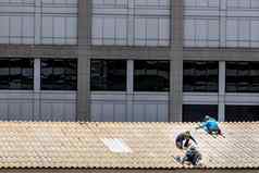 杂工工人修复瓷砖损坏的工厂屋顶