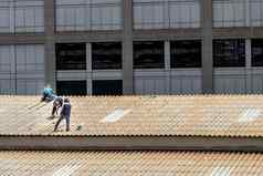 杂工工人修复瓷砖损坏的工厂屋顶