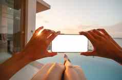 女人持有移动电话空白屏幕铺设日光浴床上海滩视图