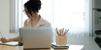 女人使笔记坐工作桌子上研究在线看网络研讨会播客移动PC听学习教育会议网络学习概念