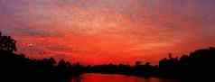 全景日落红色的天空美丽的色彩斑斓的景观轮廓树林地河反映《暮光之城》时间