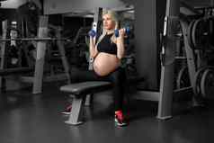 怀孕了女人提升哑铃培训肱二头肌肌肉健身房坐着板凳上