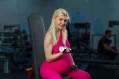 怀孕了女人提升哑铃培训肱二头肌肌肉健身房坐着板凳上