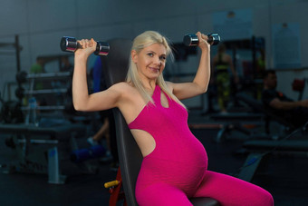怀孕了女人提升哑铃培训手臂肩膀肌肉健身房坐着板凳上
