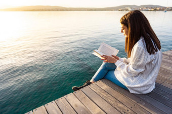 年轻的女人坐着码头日落日出透明的海海洋水阅读书学生女孩学习大学学校教训自然书狂人有趣的浪漫演讲
