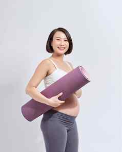 快乐的怀孕了女人持有瑜伽席微笑相机摆姿势白色背景怀孕了生活方式健身