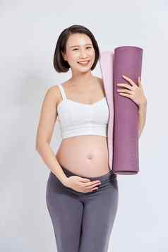 快乐的怀孕了女人持有瑜伽席微笑相机摆姿势白色背景怀孕了生活方式健身