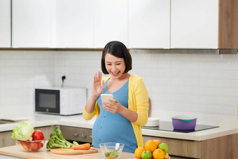 快乐怀孕了女人调用智能手机早餐首页厨房