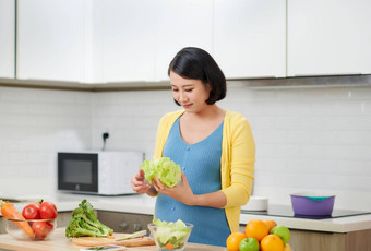 快乐怀孕了女人烹饪首页新鲜的绿色沙拉吃<strong>蔬菜</strong>怀孕健康的怀孕概念