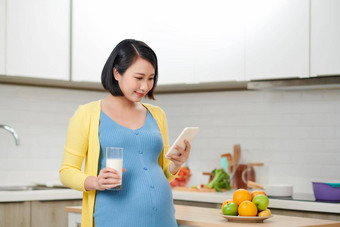 年轻的怀孕了<strong>女</strong>人持有玻璃牛奶表格食物厨房