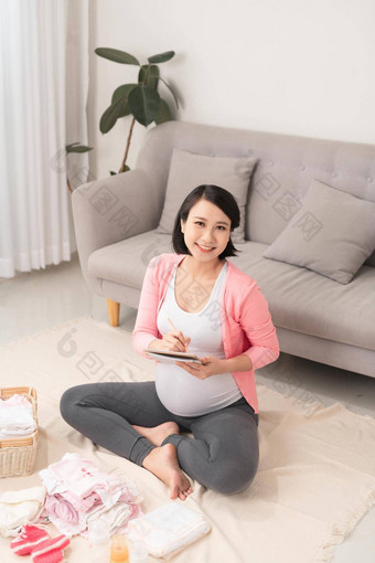 怀孕了女人首页地板上检查列表婴儿衣服准备孕妇医院