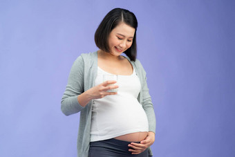 怀孕钙快乐怀孕了女人持有玻璃牛奶微笑相机站颜色背景