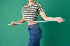 关闭年轻的女人测量腰磁带测量绿色背景