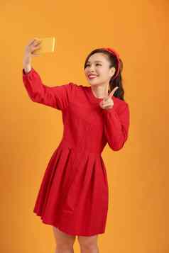 拍摄快乐年轻的亚洲女人采取自拍手机站孤立的橙色背景