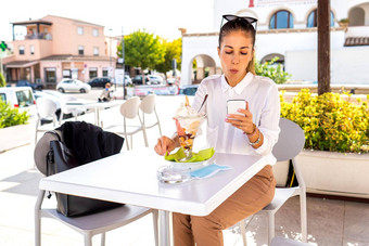 美丽的现代优雅的女人坐着税款咖啡馆酒吧表格享受大水果味冰奶油移动电话互联网连接检查电子邮件聊天社会网络