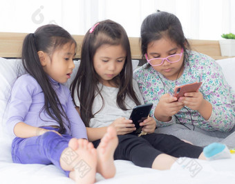 快乐亚洲孩子朋友玩智能手机沙发首页孩子们电话沙发上女孩看聪明的电话娱乐生活方式沟通概念