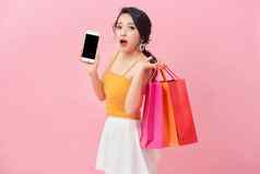 照片震惊了女人衣服智能手机手惊喜持有购物袋孤立的粉红色的背景