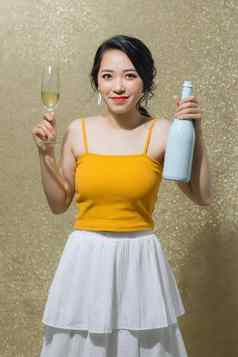 肖像快乐年轻的亚洲女人持有香槟瓶玻璃黄金背景聚会，派对概念