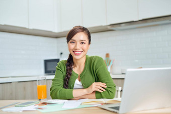 微笑年轻的女人坐桌子上厨房工作移动PC小工具快乐千禧女孩管理财务状况支付家庭支出税在线
