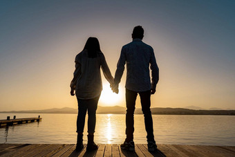暗示轮廓回来拍摄年轻的夫妇爱持有手站码头看太阳设置不断上升的地平线平海海洋水光反射积极的情感
