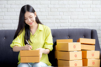 年轻的亚洲女人写作地址包裹盒子<strong>首页</strong>交付订单客户航运<strong>物流</strong>商人在线卖方业务老板锻造在线购物电子商务