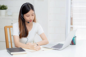 年轻的亚洲女人穿耳机研究在线电子<strong>学习</strong>桌子上女孩穿耳机<strong>学习</strong>互联网移动PC电脑首页正常的距离教育培训