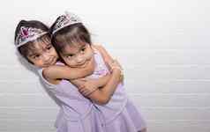 女亚洲相同的双胞胎坐着椅子白色背景穿紫色的衣服配件站拥抱
