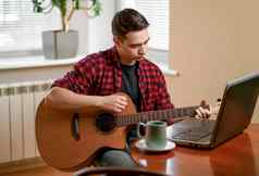年轻的男人。学习玩吉他互联网移动PC在线教训爱好休闲概念