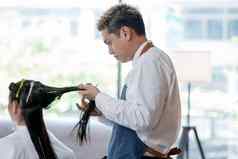 亚洲美沙龙理发师男人。过程头发减少长头发客户集中注意力工作概念美业务好人