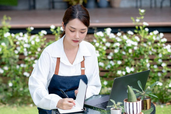 美丽的亚洲女人记录数据笔记本前面移动PC保持首页花园可持续发展的小业务联系成长植物概念