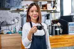 肖像咖啡师女人咖啡制造商持有杯站前面计数器咖啡商店相机微笑
