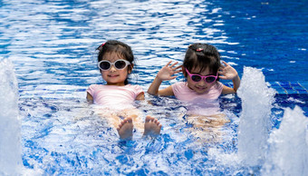 肖像漂亮的亚洲双胞胎铣削摆<strong>姿势游泳</strong>池背景穿粉红色的<strong>游泳</strong>西装太阳眼镜