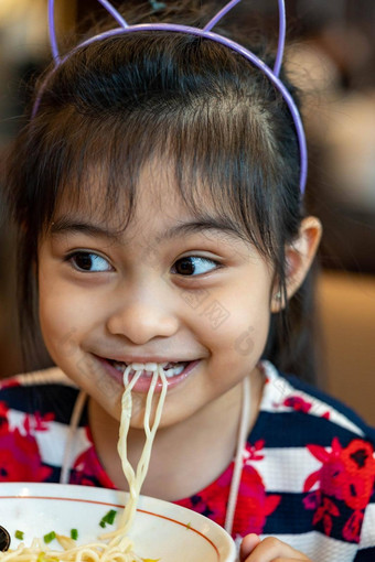 女亚洲孩子吃面条孩子吃拉面面条微笑享受食物孩子吃意大利面