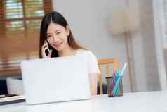 年轻的亚洲女人会说话的电话工作首页移动PC电脑自由笔记本互联网在线说话智能手机国内生活业务沟通概念