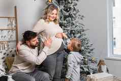 圣诞节家庭幸福肖像爸爸怀孕了妈妈儿子坐着扶手椅首页圣诞节树拥抱微笑