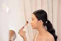 美丽的年轻的女人应用化妆镜子沙拉酱房间