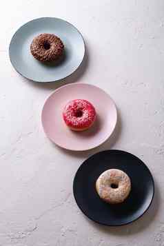 甜甜圈行盘子巧克力粉红色的香草甜甜圈洒甜蜜的上釉甜点食物白色混凝土变形背景角视图