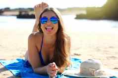 年轻的有吸引力的女人太阳镜说谎沙子海滩显示舌头相机