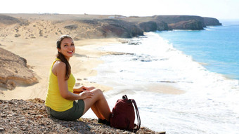美丽的年轻的背包客坐着享受视图海洋波相机playa游船上海滩兰斯洛特金丝雀岛屿西班牙