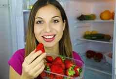关闭美丽的微笑女孩冰箱持有草莓手相机健康的食物概念新鲜的水果蔬菜
