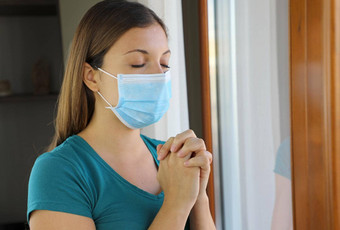 科维德流感大流行冠状病毒女人祈祷穿面具病毒萨尔斯科夫女孩关闭眼睛祈祷窗口穿外科手术面具脸冠状病毒疾病