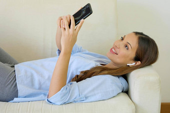年轻的有吸引力的女人放松沙发上首页选择音乐聪明的电话听音乐无线耳机