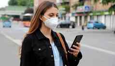 科维德年轻的女人穿断续器面具聪明的电话应用程序软件城市街援助联系跟踪诊断响应流感大流行冠状病毒