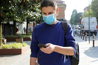 科维德流感大流行冠状病毒担心年轻的男人。穿外科手术面具聪明的电话应用程序城市街援助联系跟踪诊断响应冠状病毒流感大流行