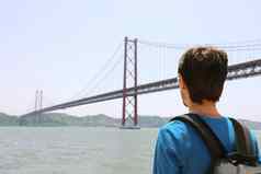 回来视图年轻的背包客男人。桥旅行者旅游背包海滨里斯本葡萄牙4月桥