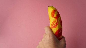 女人手持有香蕉红色的口红标记粉红色的背景