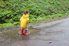 好玩的女孩穿黄色的雨衣跳水坑降雨