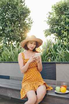 年轻的亚洲女孩智能手机公园穿黄色的衣服他夏天概念