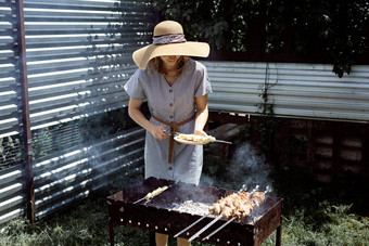 年轻的女人夏天他烧烤肉在户外后院